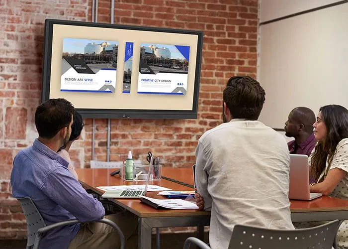 a group of people around a conference room table all look at a presentation on a ViewBoard mounted on the wall