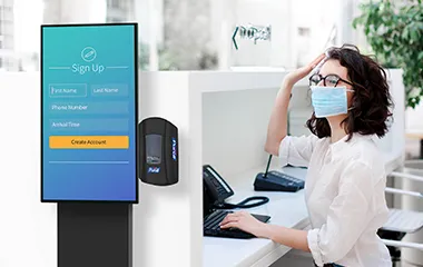 Woman working at a desk near an information kiosk with hand sanitizing station