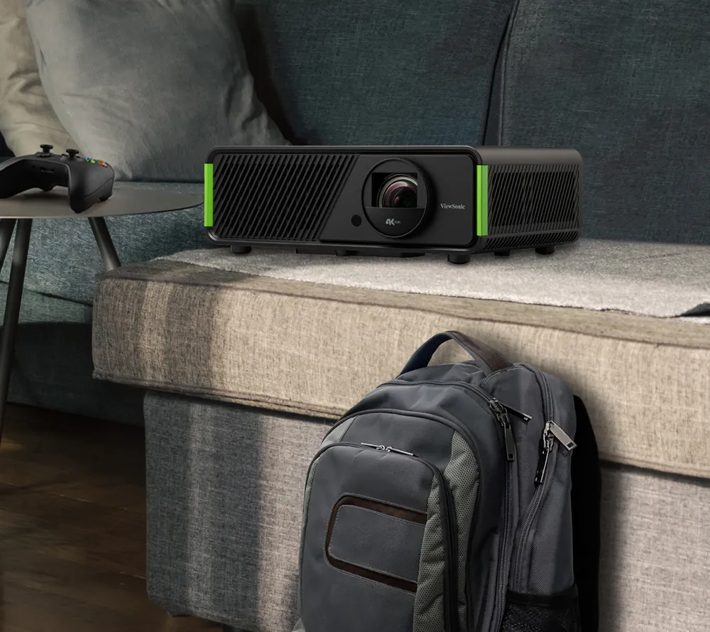 X2-4K projector sitting on a couch and next to a backback