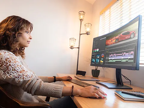 a woman working on a video editing timeline on an ultrawide monitor