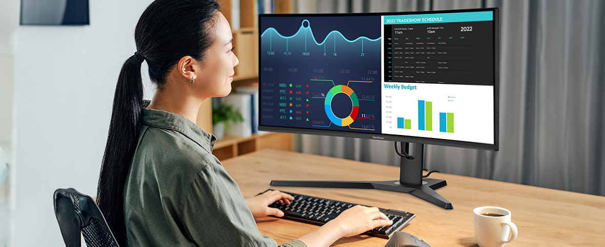 a woman with multiple windows of charts and graphs open on an ultrawide monitor 
