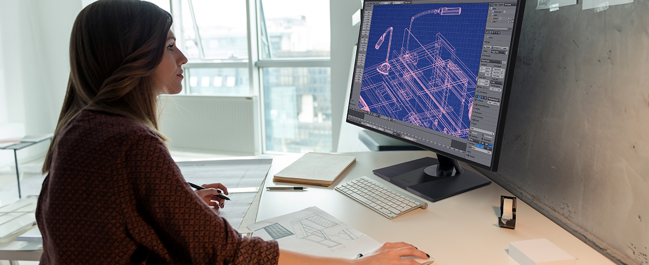 a woman sits at a desk full of papers editing a building wireframe model