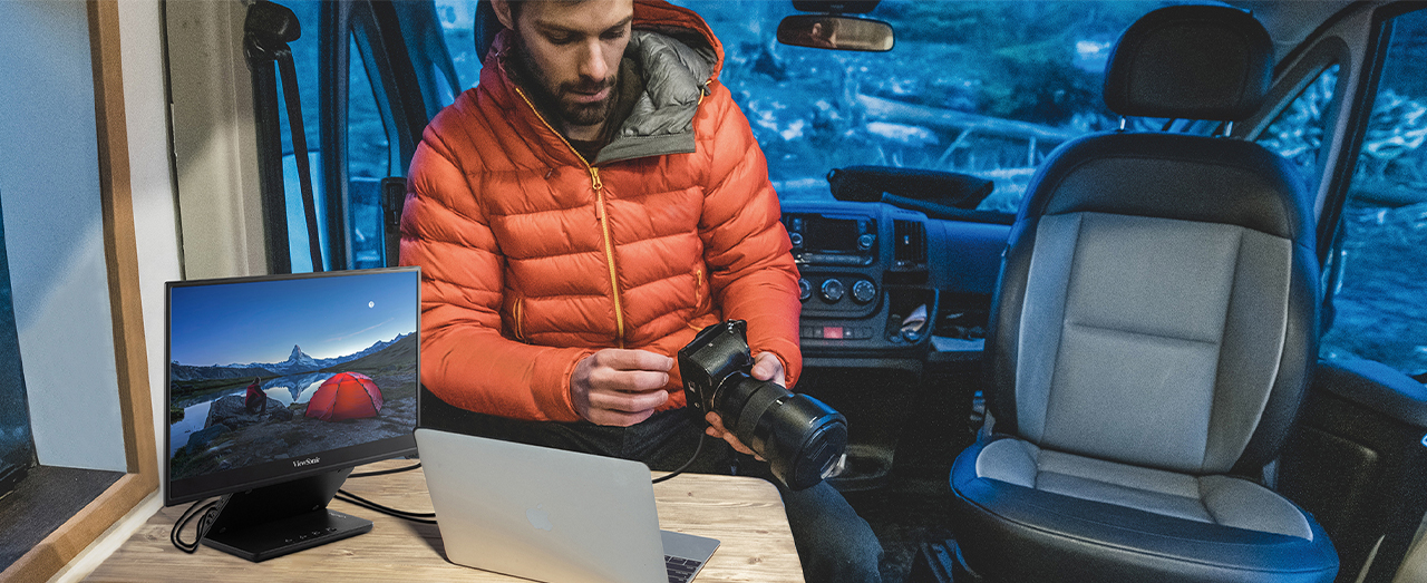 aa man sits in the back of a van holding a camera with a portable monitor plugged in to his laptop