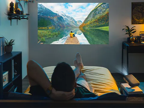 someone watches a projected image on their wall from bed