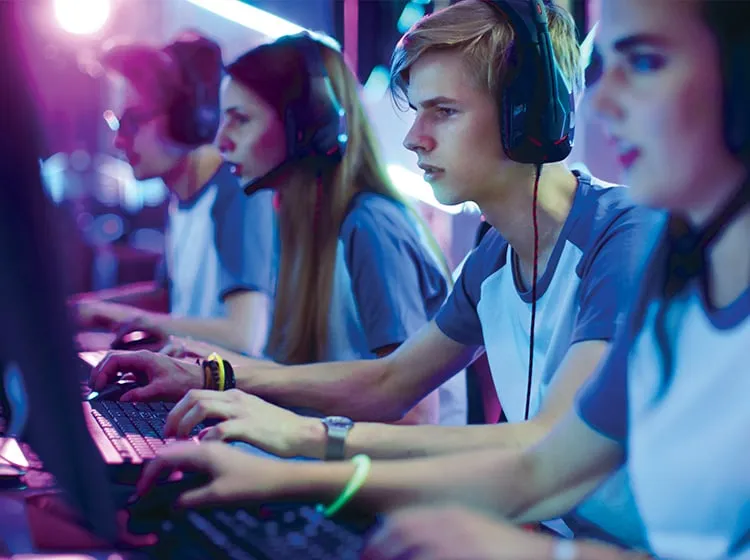 teens in uniform wearing headsets playing at an esporting event alongside their team mates
