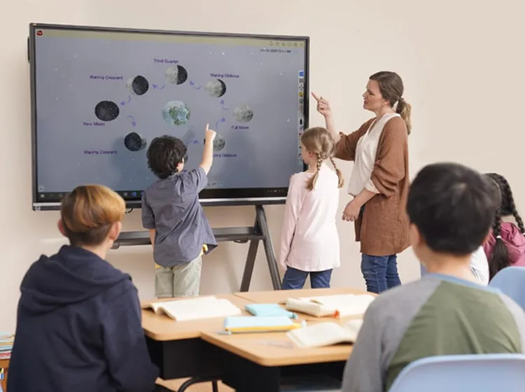 students at an interactive whiteboard display along with a teacher during a presentation