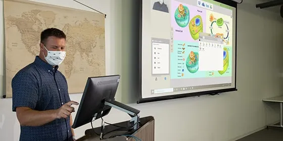 man instructing in front of a room on a small touch screen display