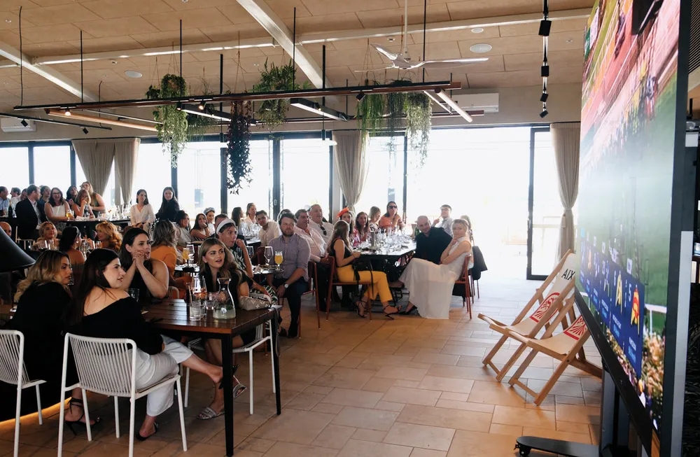 a group of people remotely watching a sporting event on a large screen in a venue