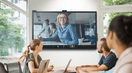 Employees with laptops sitting in a meeting room using a ViewBoard to collaborate with a coworker.